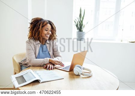 Young African American Woman Is Working On A Laptop. Happy Female Student Is Looking At Computer Scr