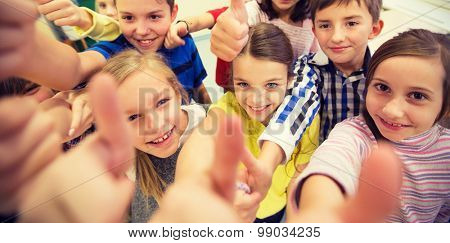 education, elementary school, learning, gesture and people concept - group of school kids and showing thumbs up in classroom