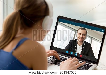 Man and woman in headphones communicating online by video call, looking at full screen videoconferencing app window, webcam videochat, virtual dating, long distance relationships, close up rear view