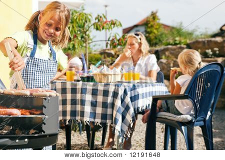 Family having a barbecue party - little kid at the barbecue grill preparing meat and sausages