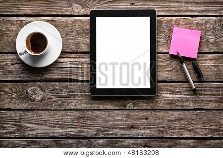 Digital tablet computer with sticky note paper and cup of coffee on old wooden desk. Simple workspace or coffee break with web surfing.