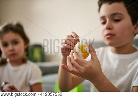 Boy Decorating An Easter Egg With Yellow Gouache. Closeup Of Hands On The Background Of Blurry Child