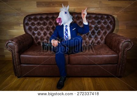 Funny Unicorn In Elegant Suit Siting On Sofa Like A Boss And Showing Hand Gesture With Raised Index 