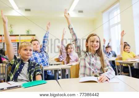 education, elementary school, learning and people concept - group of school kids with notebooks sitting in classroom and raising hands