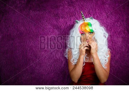 Freaky Young Woman In Unusual Wig Stands On The Purple Background. Portrait Of Handsome Lady In Red 