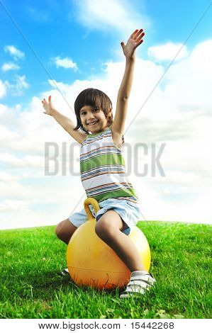 Sporty cute positive kid, playing happily with big ball on green meadow