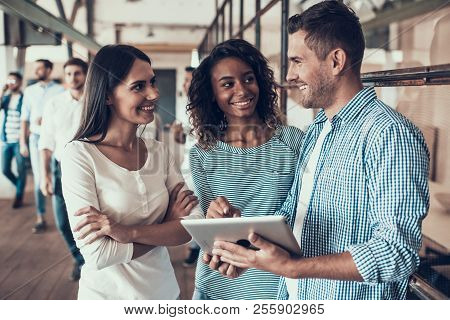 Group Of Young Business People Using Tablet. Young Smiling Man Showing Project On Tablet To Colleagu