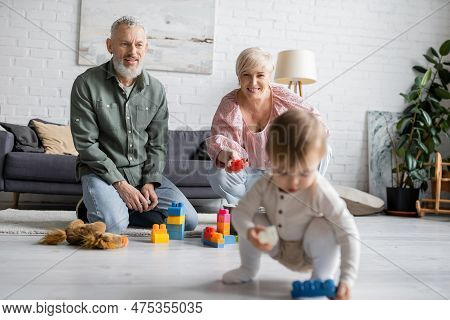 Happy Middle Aged Grandparents Sitting On Floor Near Building Blocks While Little Girl Playing With 