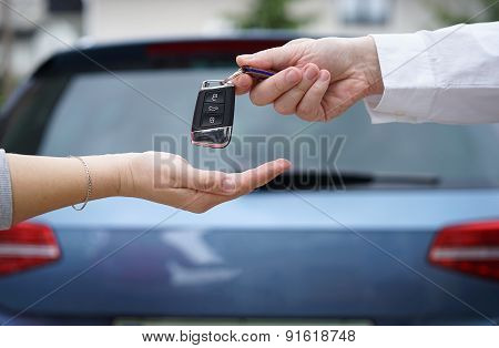 Car Dealer Gives The Customer The Car Keys With Car In Backgorund