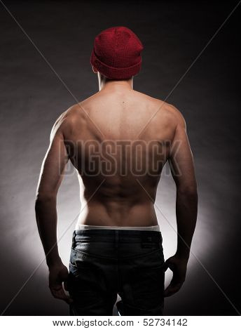 Shirtless back of a young fit and muscular man wearing a beanie hat in a dark background