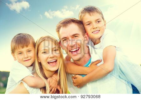 Happy joyful young family father, mother and kids having fun outdoors, playing together outside. Mom, Dad and kid laughing and hugging, enjoying nature. Sunny day, good mood