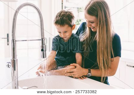 Mother with her child playing with water in kitchen sink at home. Happy lifestyle family moments.