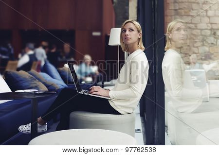 Thoughtful female person sitting in modern coffee shop interior with open laptop computer