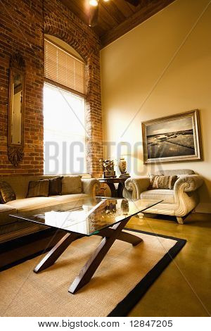 Interior of living room with large window, brick wall, coffee table, and sofa.