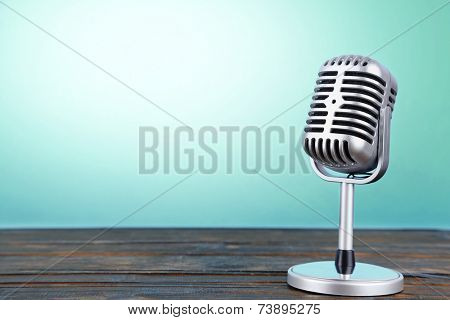 Old metal microphone on wooden table on light blue background