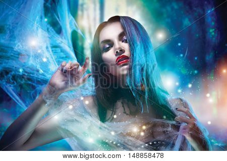 Beautiful Halloween Vampire Woman portrait. Beauty Vampire Vitch lady with blood on mouth posing in deep forest, wearing spider web. Fashion Art design. Sexy model girl with Halloween make up