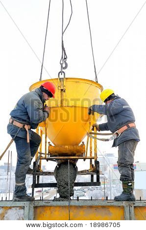 Two construction building workers at construction site pouring concrete in mould